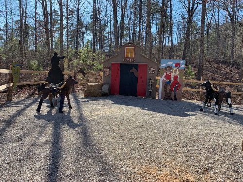 A rustic livery with wooden horse cutouts, hay bales, and a colorful mural in a wooded area.