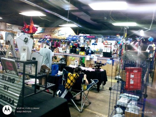 A bustling indoor market with various stalls selling merchandise, including clothing and accessories.