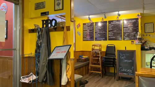 Interior of a casual eatery with yellow walls, a menu board, seating, and BBQ-themed decor.