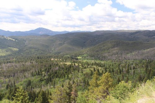 A panoramic view of lush green mountains and valleys under a partly cloudy sky.