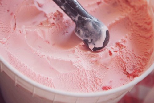 A close-up of a tub of pink ice cream with a black scoop resting on top.