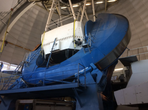 Large blue telescope structure inside an observatory, with a domed ceiling and support equipment visible.