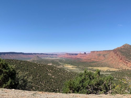 A panoramic view of a desert landscape with red rock formations, green vegetation, and a clear blue sky.
