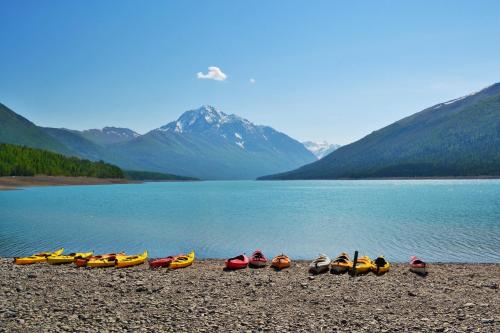 Colorful kayaks lined up on a rocky shore, with a serene lake and snow-capped mountains in the background.
