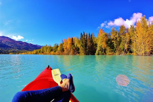 A person relaxes in a kayak on a calm lake, surrounded by vibrant autumn trees and a clear blue sky.