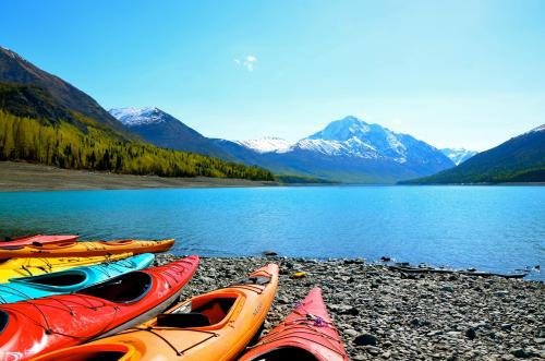 Colorful kayaks lined up on a rocky shore, with a serene blue lake and snow-capped mountains in the background.