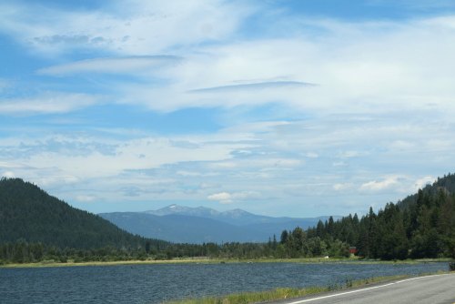 A scenic view of a lake surrounded by mountains and trees under a partly cloudy sky.