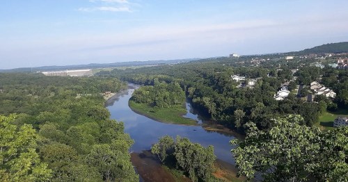 A scenic view of a winding river surrounded by lush greenery and a small town in the distance under a clear blue sky.