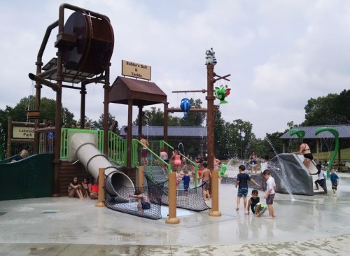 A vibrant water play area with slides, nets, and children playing in the water under a cloudy sky.