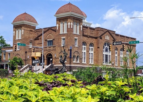 Historic brick building with domed roofs, surrounded by greenery and street signs, under a blue sky.