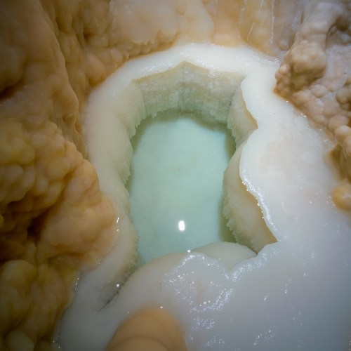 A close-up of a mineral formation with a small, clear pool of water surrounded by creamy, textured deposits.