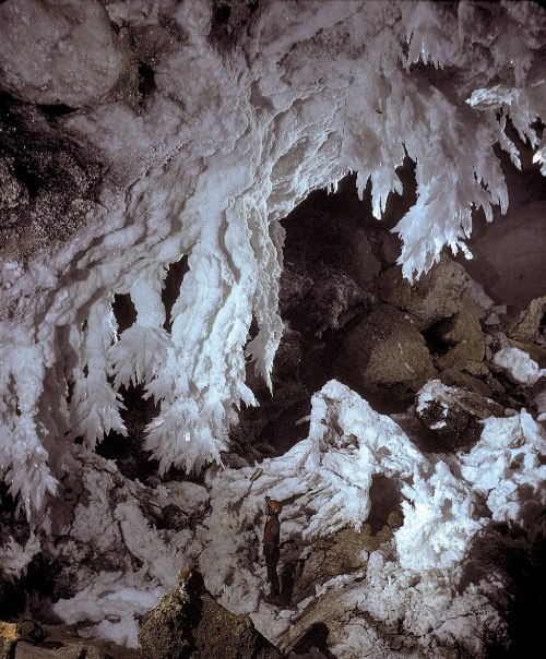 A person stands in a cave surrounded by stunning white ice formations and crystalline structures.