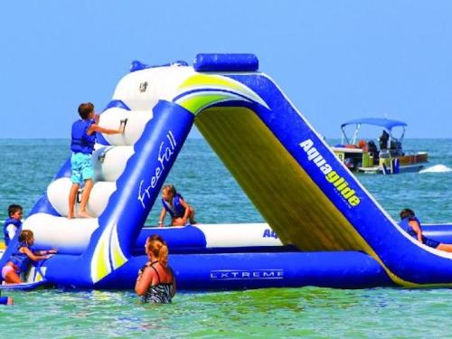 Children play on a large inflatable water slide in the ocean, with a boat in the background.