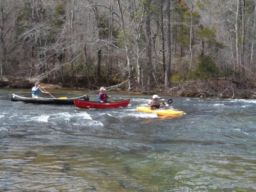 Three people kayaking and canoeing on a river surrounded by trees in a natural setting.
