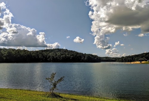 A serene lake surrounded by green hills under a blue sky with fluffy clouds.