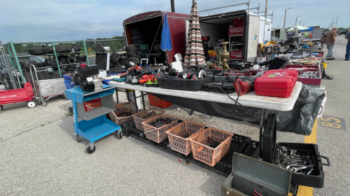 A bustling outdoor market scene with tables filled with various tools, equipment, and storage bins.