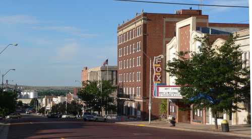 A street view of a small town featuring brick buildings, a theater marquee, and a clear blue sky.