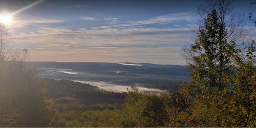 A scenic view of rolling hills and valleys shrouded in mist, with a bright sun shining in the sky.