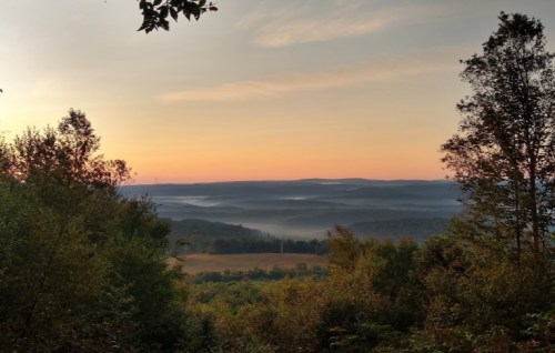 A serene landscape at sunrise, with misty valleys and rolling hills under a colorful sky.