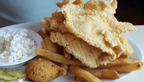 A plate of fried fish fillets, French fries, coleslaw, and a cornbread muffin.