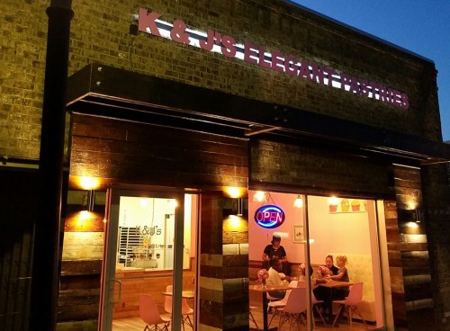 Exterior view of K&J's Elegant Pastries at night, featuring an open sign and patrons dining inside.