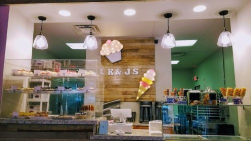 A colorful ice cream shop display with desserts, a wooden wall, and pendant lights illuminating the counter.