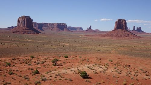 A vast desert landscape featuring iconic red rock formations and mesas under a clear blue sky.