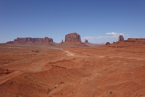 A vast desert landscape with red rock formations under a clear blue sky.