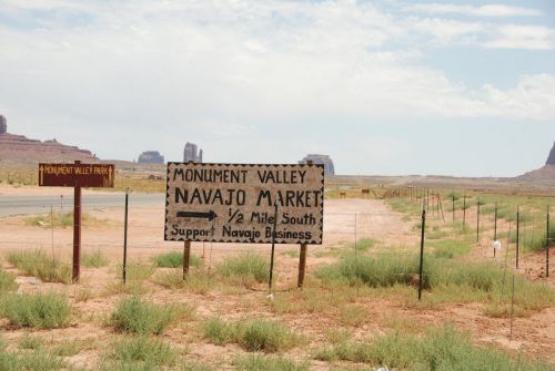 Sign for Monument Valley Navajo Market, indicating it's half a mile south, with desert landscape in the background.