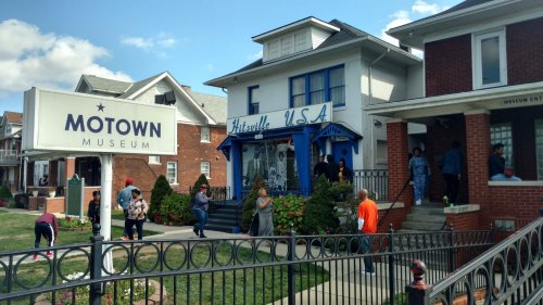 Exterior of the Motown Museum, with visitors outside and a sign reading "Hitsville U.S.A." on a sunny day.