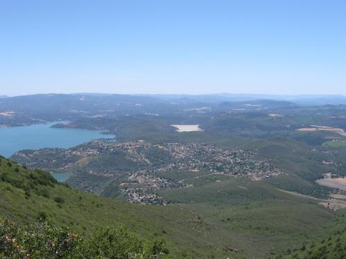 A panoramic view of a lush green landscape with a lake and small town nestled in the valley under a clear blue sky.