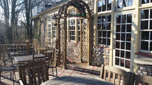A stone building with large windows and a wooden deck, featuring outdoor tables and a smoke-free sign.