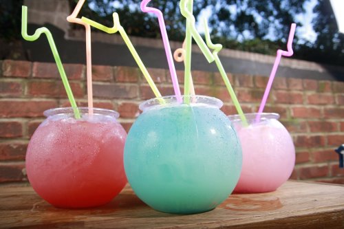 Three colorful drinks in round bowls with vibrant straws, set against a brick background.