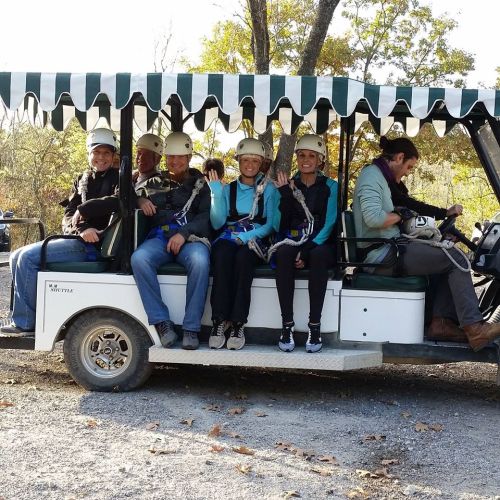 A group of six people in helmets sits on a golf cart, ready for an outdoor adventure. A guide is driving.