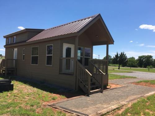 A small, modern house with a metal roof, front porch, and green lawn under a clear blue sky.