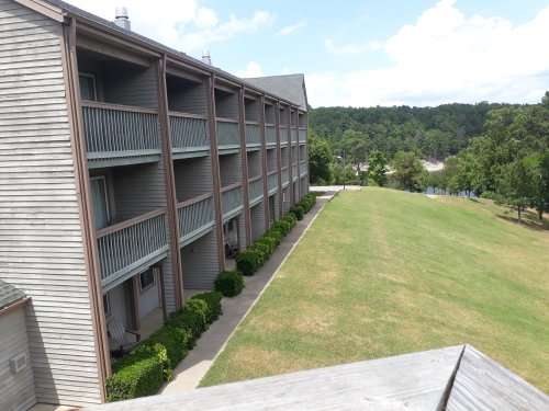 A view of a multi-story building with balconies, surrounded by a grassy area and trees in the background.