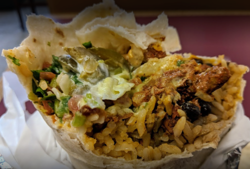 A close-up of a burrito filled with rice, beans, lettuce, and meat, wrapped in a tortilla.