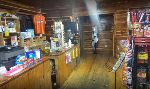Interior of a rustic convenience store with wooden walls, shelves of snacks, and a checkout counter.