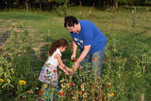 A woman and a young girl are picking flowers together in a sunny garden filled with colorful blooms.