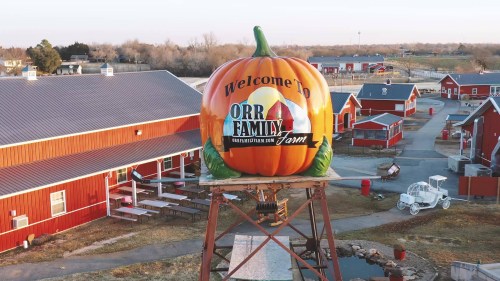 A large pumpkin sign welcomes visitors to Orr Family Farm, surrounded by red barns and open fields.