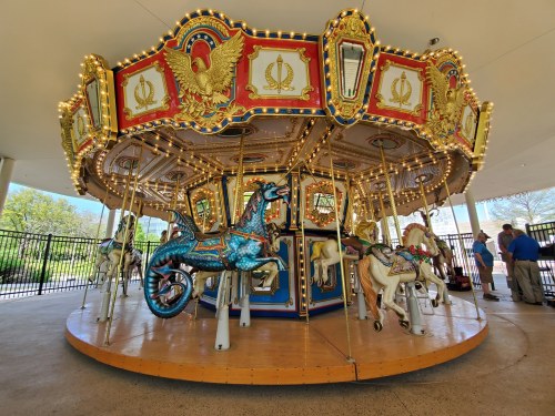 A colorful carousel with ornate decorations and illuminated lights, featuring various painted horses and a blue horse.