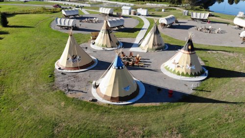 Aerial view of several colorful tipis arranged in a grassy area, with picnic tables and a pathway nearby.