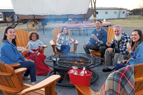 A group of six people sitting around a fire pit, enjoying snacks and each other's company in a cozy outdoor setting.