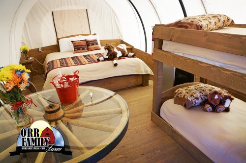 Cozy interior of a family glamping tent with a double bed, bunk beds, and a round table with flowers.