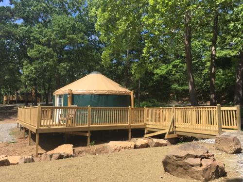 A wooden deck surrounds a green yurt in a wooded area, with rocks and gravel in the foreground.