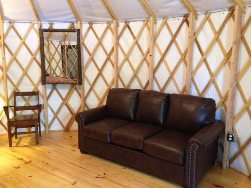 Interior of a yurt featuring a brown leather couch, a wooden chair, and a mirror against a lattice wall.