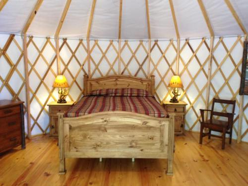 Cozy yurt interior featuring a wooden bed, nightstands with lamps, and rustic wooden furniture.