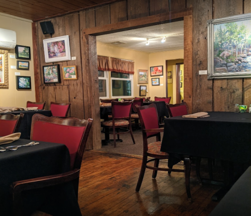 Cozy restaurant interior with wooden walls, tables set for dining, and colorful artwork on the walls.