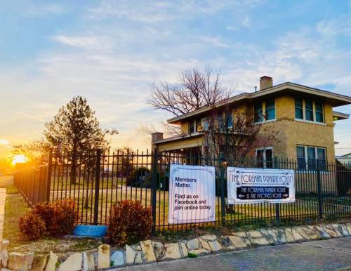 A brick building with a fence, featuring a sign about membership and a sunset in the background.