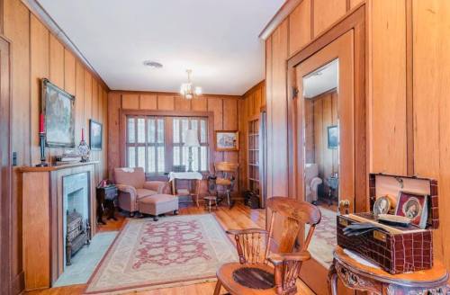 Cozy room with wooden walls, a fireplace, armchair, and vintage decor, featuring a large mirror and a patterned rug.
